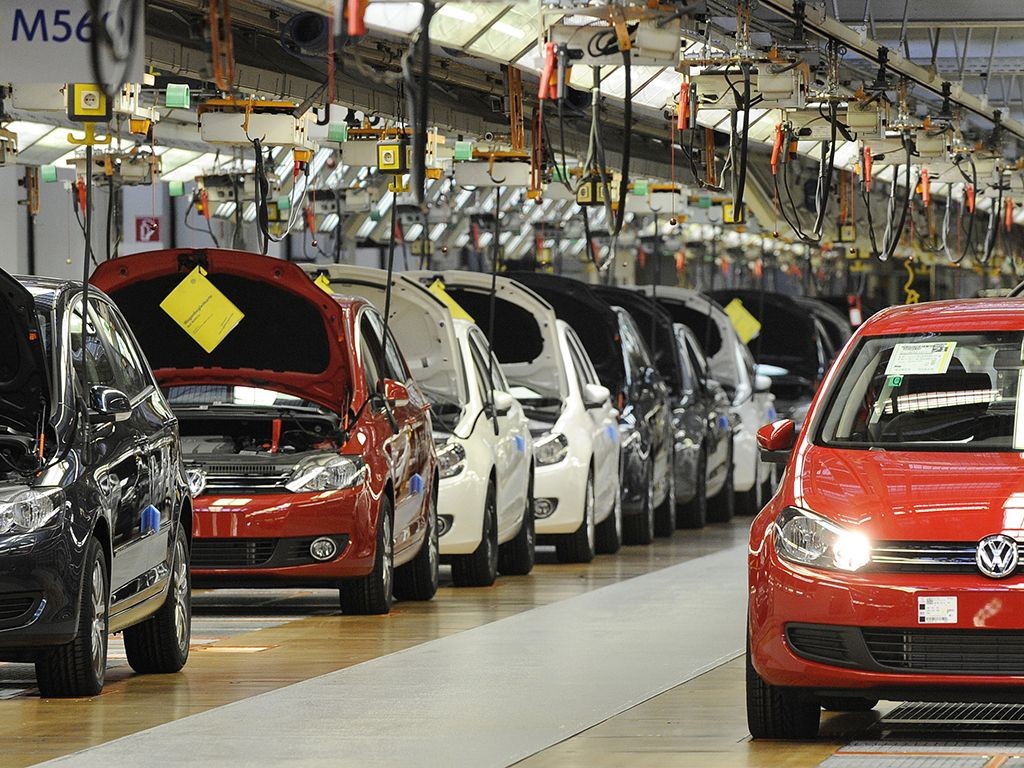 Assembly line with multiple cars in various stages of production inside a factory.