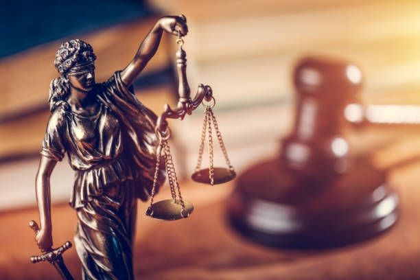 Bronze statue of Lady Justice holding scales, with a judge's gavel in the background.