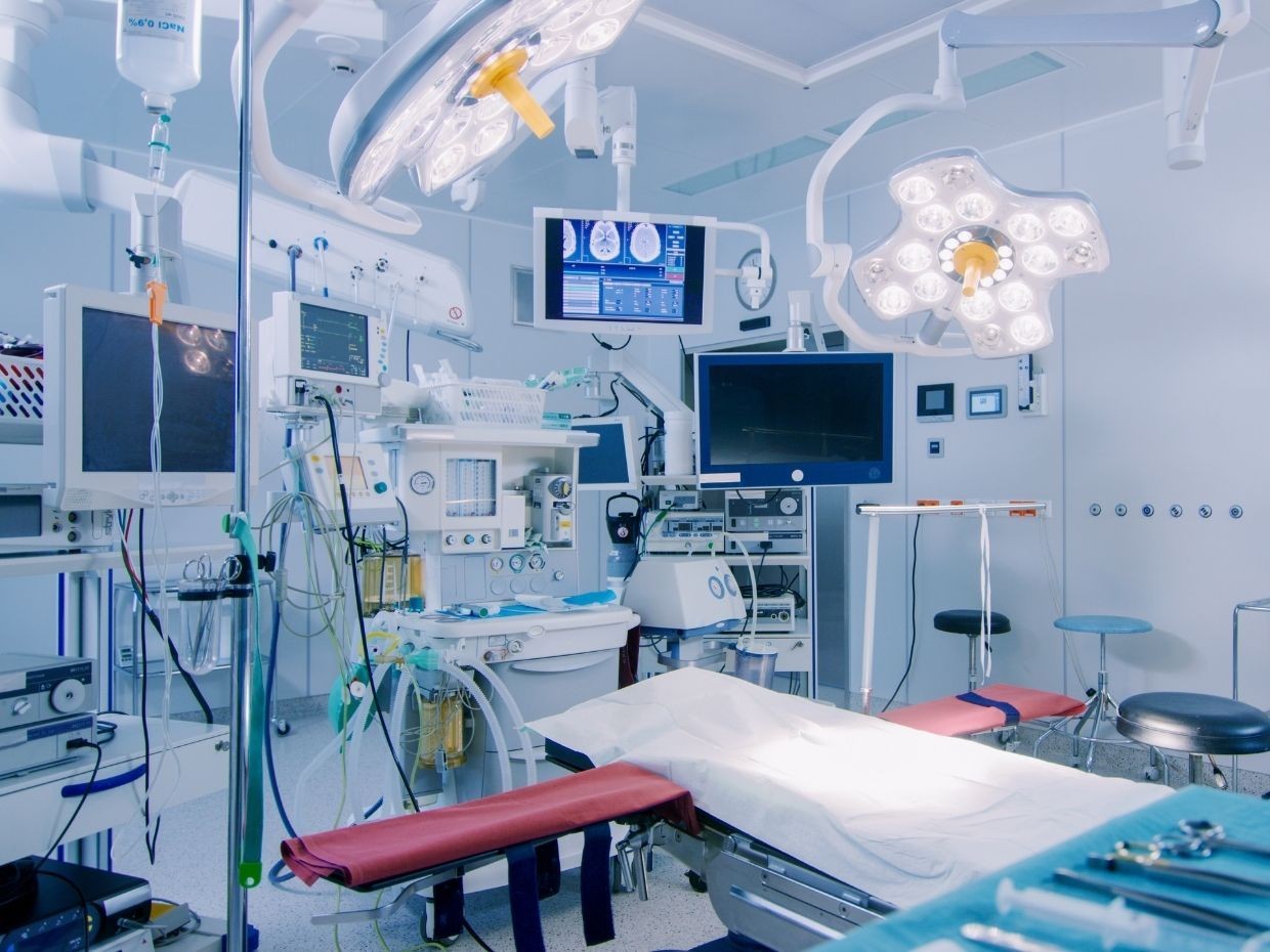 Modern surgical operating room with advanced medical equipment, monitors, and bright overhead lights illuminating the area.